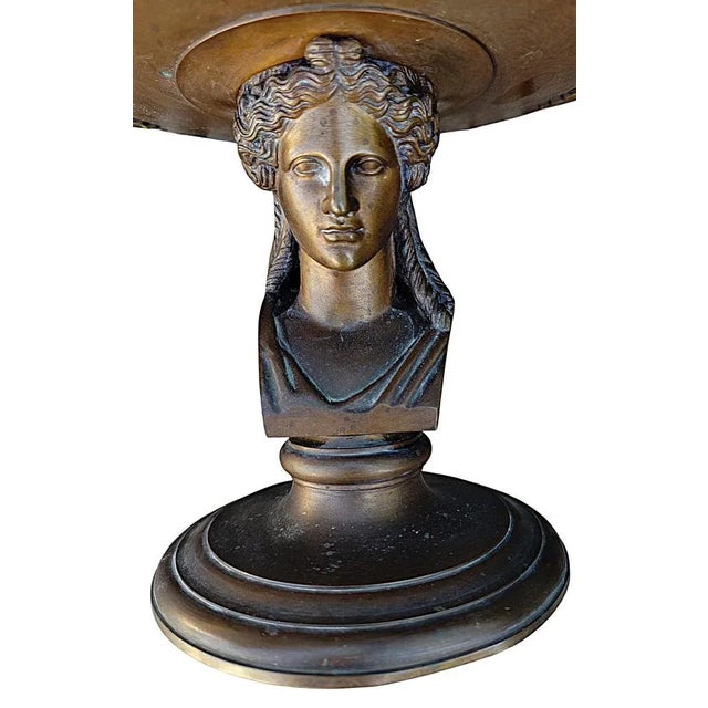 Bronze cup supported by a bust of an antique woman, resting on a pedestal. The exterior is decorated with a wolf...