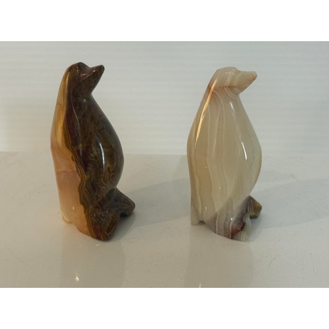 A charming vintage pair of hand-carved penguin figurines executed in translucent banded natural stone, likely alabaster or...