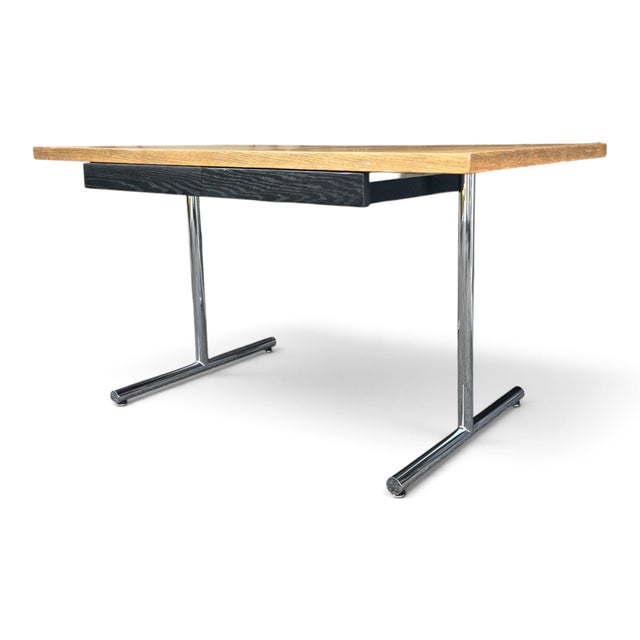Defined by its bold contrast of warm wood, ebonized black, and polished chrome, this Mid-Century Modern writing desk...