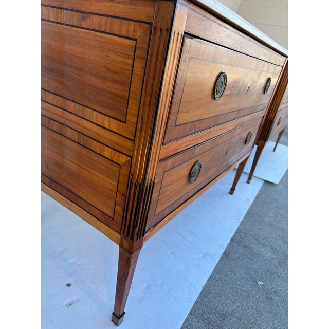 A pair of Louis XVI-style, marble-topped commodes from France (late 19th century) in ebonized accents, with large drawers,...
