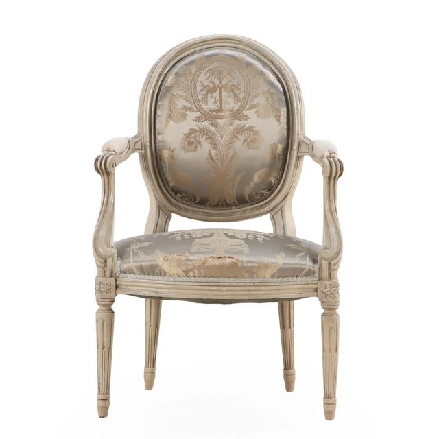 The painted and carved frames with oval padded backs, small arm rests, and seats supported by turned and fluted legs....