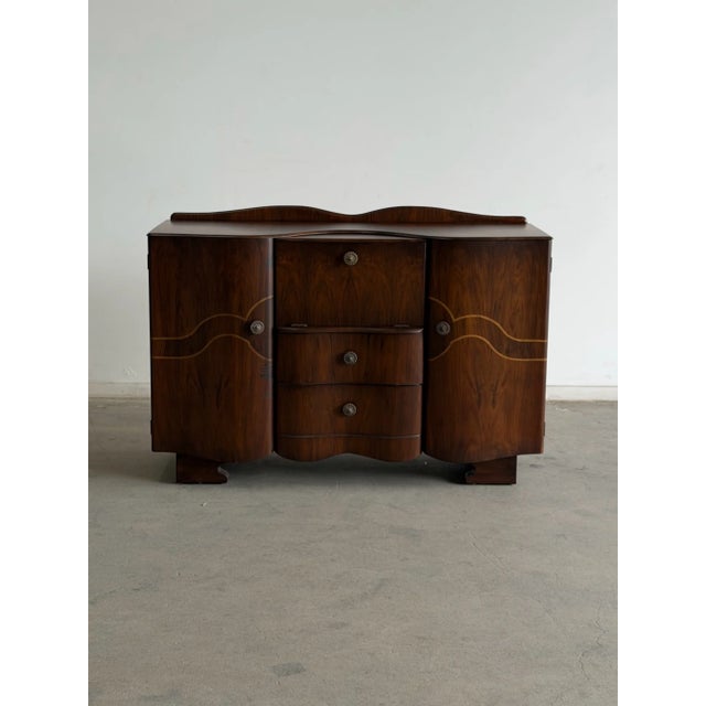 W54.5 D19.25 H37.25 A striking vintage Art Deco sideboard featuring a classic waterfall silhouette, flowing wood grain,...
