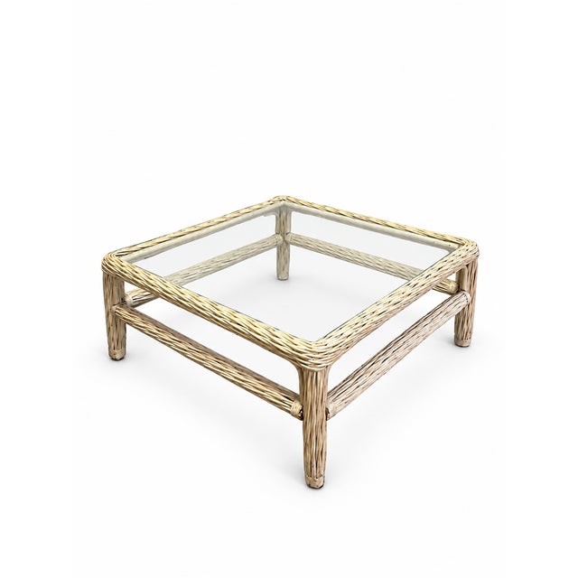 A charming late-20th-century square coffee table featuring a woven wicker and rattan frame with an inset clear glass top....