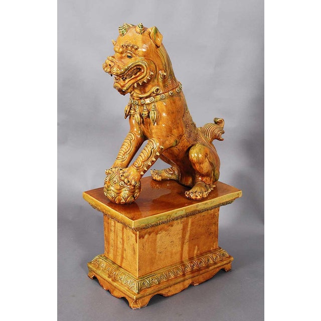 A pair of large terra cotta foo dogs in a yellow and green glaze. Depicting the typical male and female forms and raised...