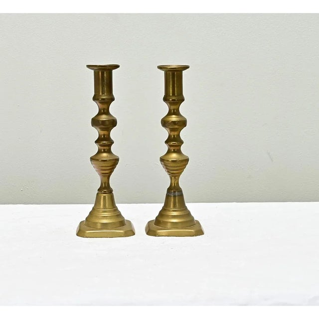A pair of French vintage brass candlesticks with turned columns on squared pedestal bases, patina consistent with age and...