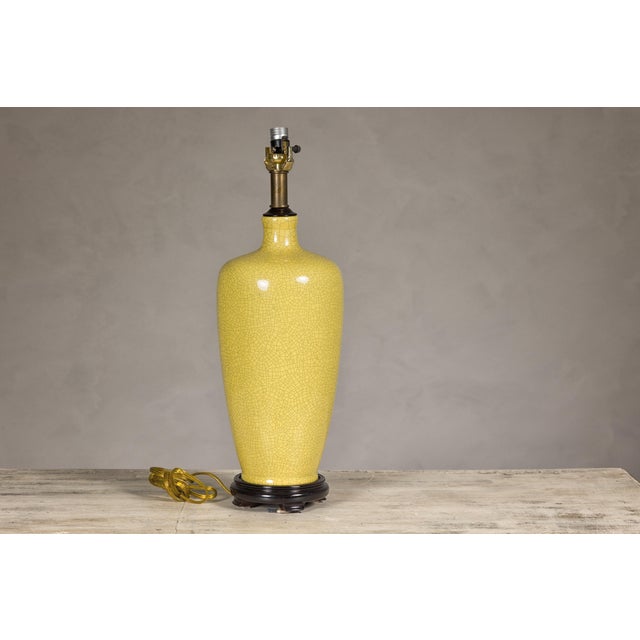 A crackle yellow glazed ceramic vase made into a table lamp and mounted on a circular wooden base with petite feet. This...