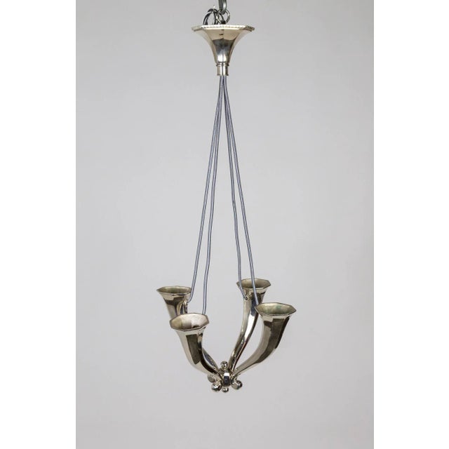 A solid, understated, shining silver chandelier with four upward facing, horn shaped arms. Recessed sockets have a clean...