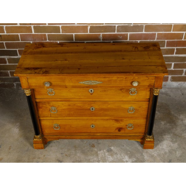 A French Empire fruitwood four-drawer commode from the early 19th century with ebonized columns, gilt Corinthian capitals...