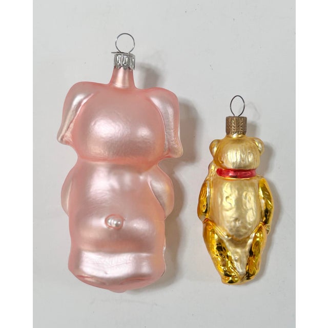 Pair of vintage German glass Christmas ornaments featuring a cheerful pink pig and a golden teddy bear. The oversized pig...