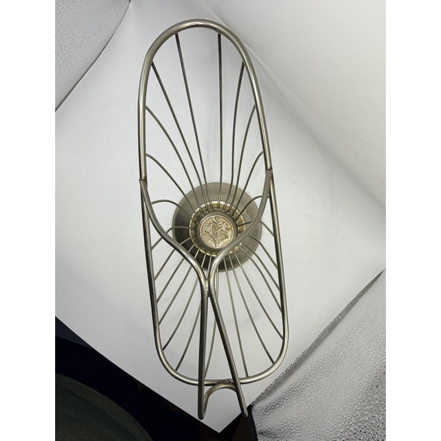 This elegant vintage metal wine bottle holder features a sculptural wire-frame cradle resting on a raised pedestal base....