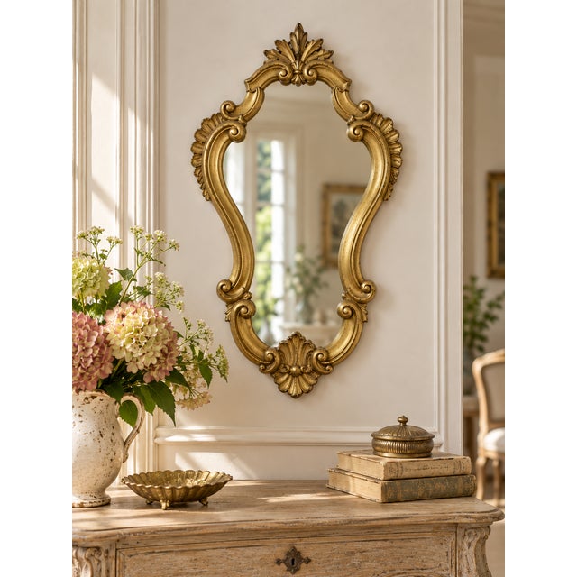 An elegant vintage wall mirror featuring a richly ornamented, Rococo-inspired frame with graceful scrolling curves,...