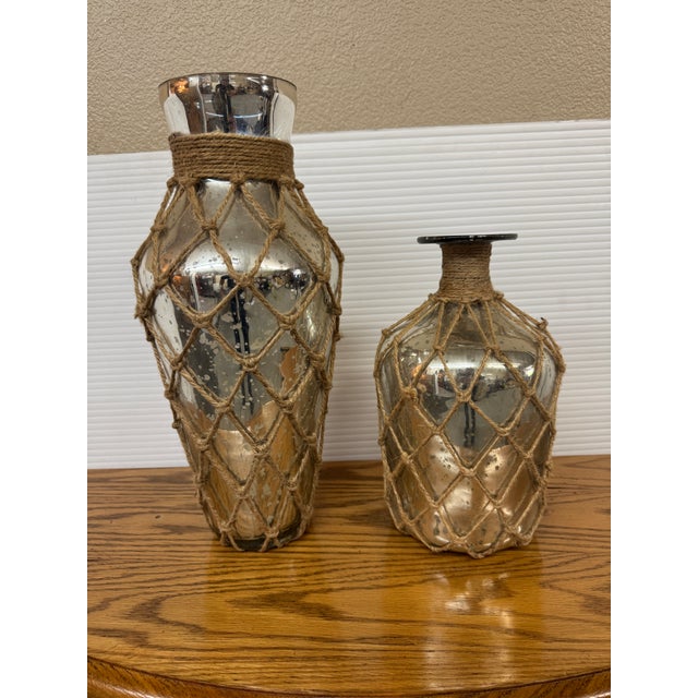 Design Plus Gallery presents a Set of Two Mercury Glass Jugs Wrapped in Jute. Their design has a distinctive antique...