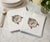 Vintage hand-embroidered cotton dinner napkins featuring delicate cross-stitch floral motifs and distinctive blue stitched...