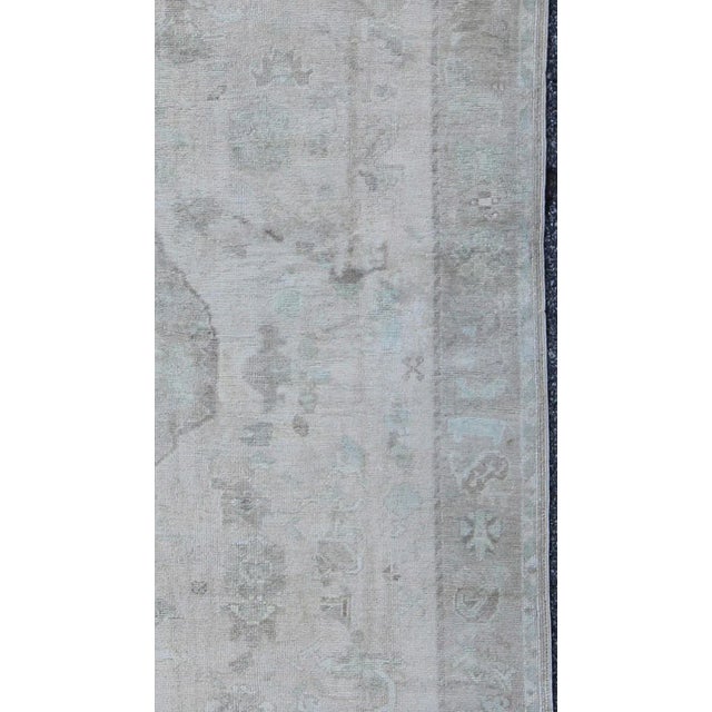 This Oushak rug features a unique blend of colors and an intricately beautiful design. The multi-layered Sub-geometric...