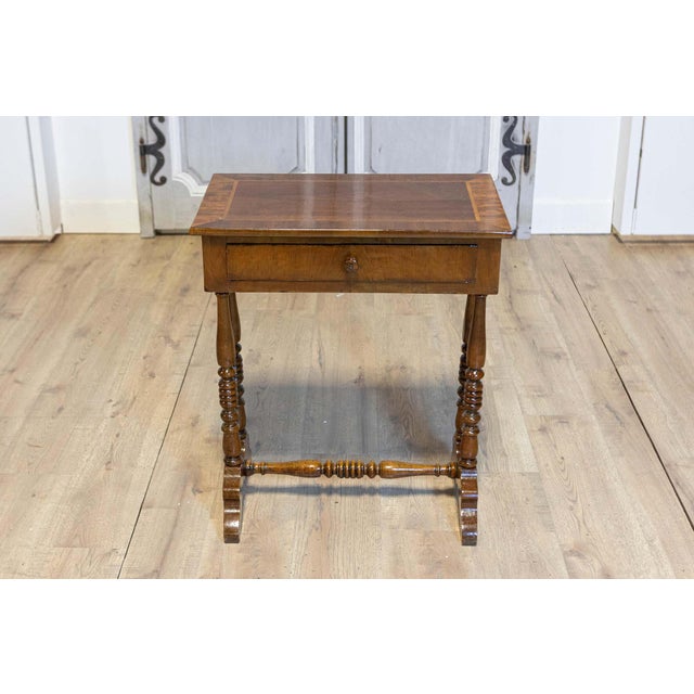 An Italian walnut side table from the 19th century with inlaid banding, single drawer, turned trestle base and cross...