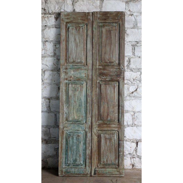 A striking pair of antique double barn doors featuring intricate floral hand carvings and a beautifully distressed blue...