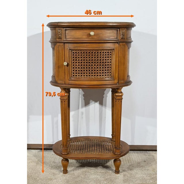 This small barrel table in light walnut-colored beech opens at the waist with a knockout drawer with a chiseled brass lens...