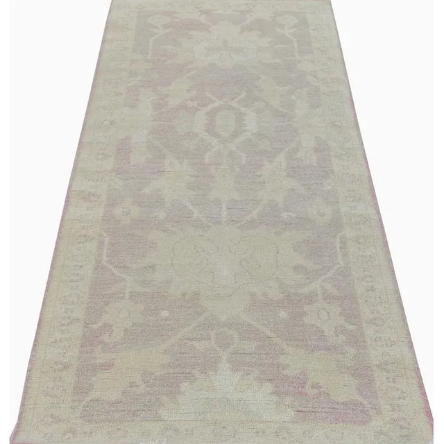 This traditional handwoven Oushak style area rug features a recreated Vintage design. The elegant light pink colored field...