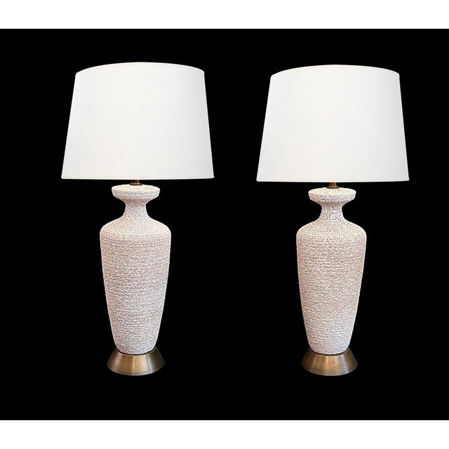 each tall lamp with everted neck above a tapering body all in a textured ivory and tan surface; raised on patinated metal...