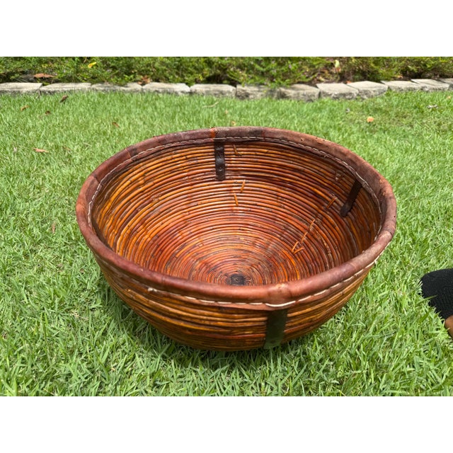 Handwoven pencil rattan basket featuring a substantial rounded form with leather-wrapped rim and hand-forged iron...