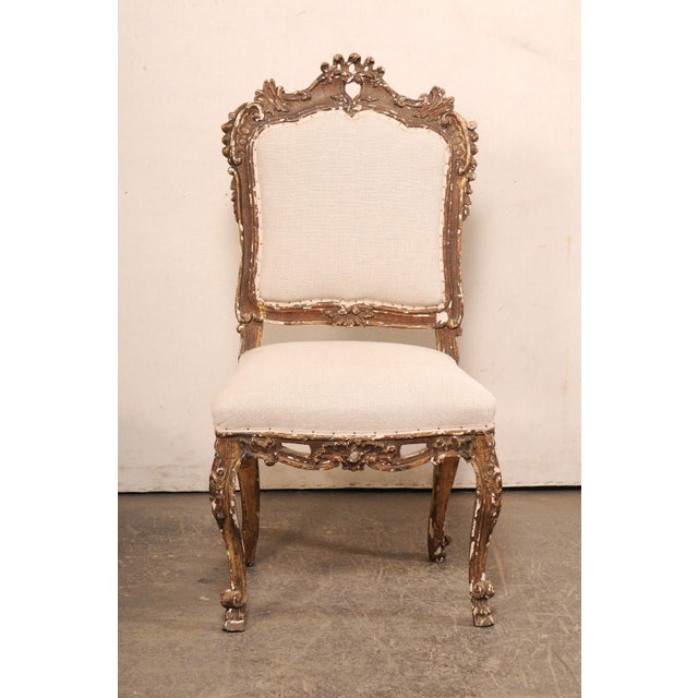 An Italian Venetian pair of richly-carved wood side chairs with upholstered seats from the 18th Century. This pair of...