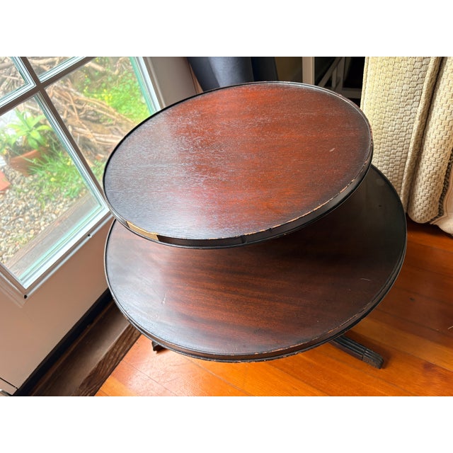A commanding two-tier mahogany dumbwaiter table with a turned pedestal column connecting two circular tray tops, raised on...