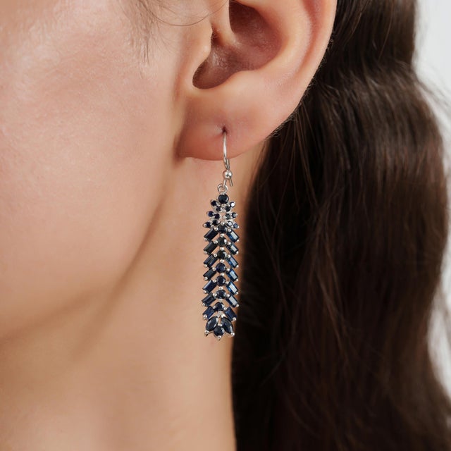 These Art Deco-inspired drop earrings are crafted in 925 sterling silver and feature 5.48 carats of blue sapphires in a...