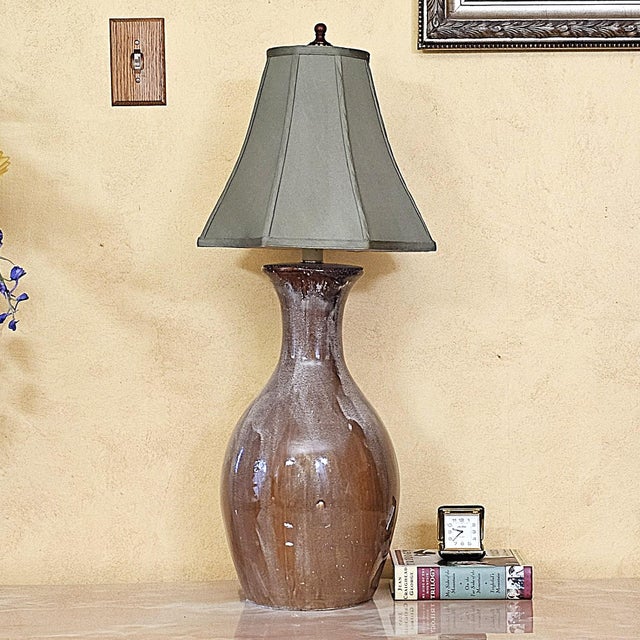 Vintage ceramic table lamp featuring a classic bottle-form body with a rich brown drip-glaze finish, wood-tone finial, and...