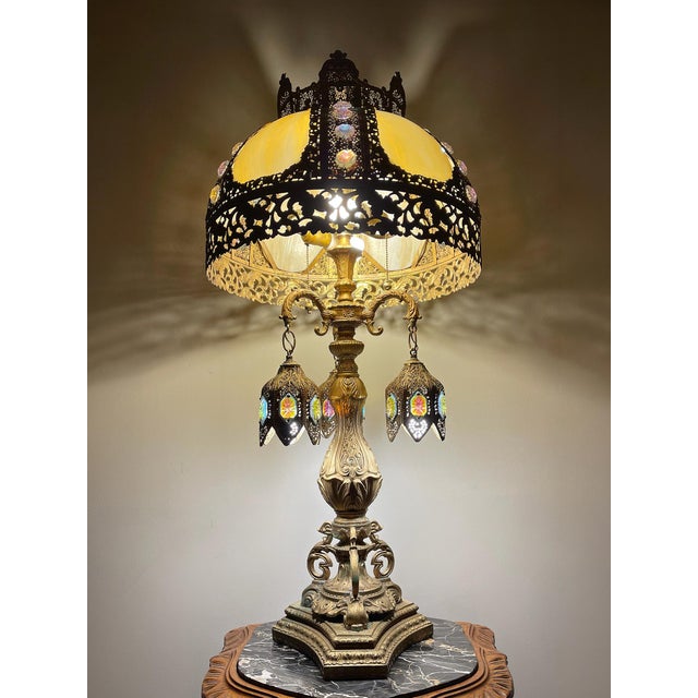 A grand vintage statement table lamp with a dramatic jeweled slag glass shade, ornate filigree metalwork, and three...
