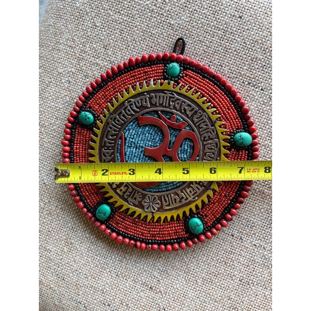 Handcrafted decorative wall hanging OM plaque featuring red, blue, orange and turquoise beads with a central metallic Om...