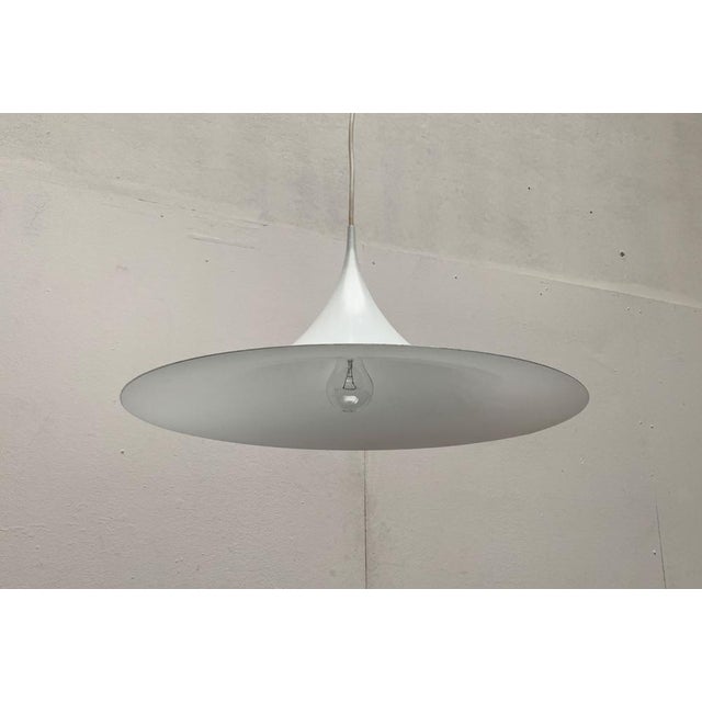 Semi pendant lamp in white. Elegant shape, narrow in profile. The entire shape of the luminaire runs together in a finely...