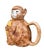 A utterly charming and expertly crafted majolica teapot in the form of a wide-eyed monkey clutching an oversized yellow...
