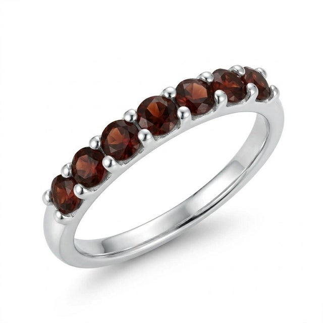 This elegant band ring features a row of rich Garnet gemstones, admired for their deep red hue and captivating brilliance....