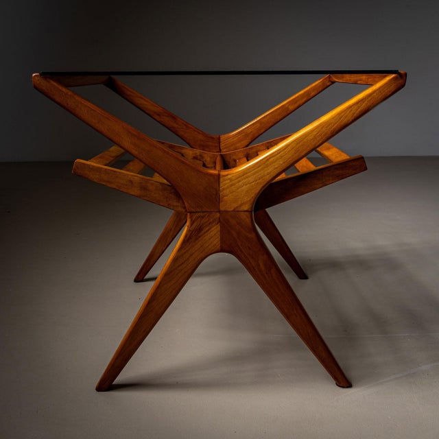A stylish mid-20th century Italian side table featuring a smooth wood frame with a sleek glass top. The table's X-shaped...
