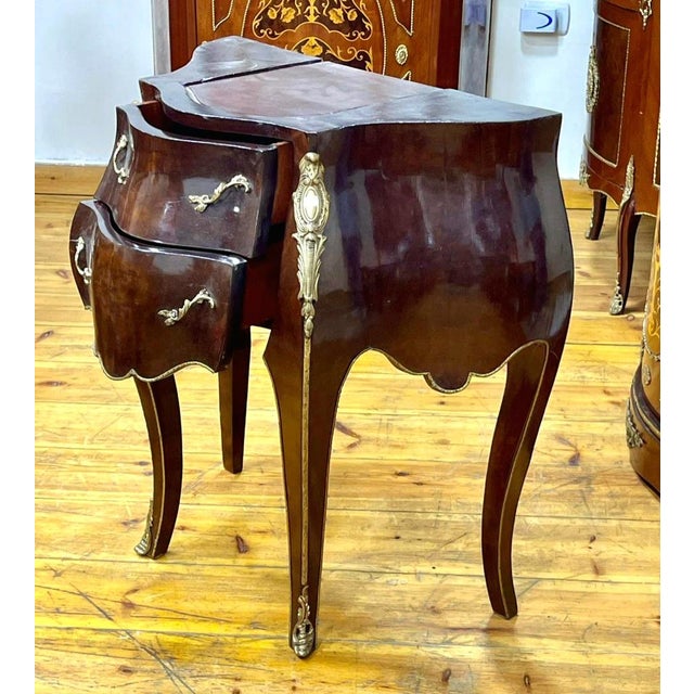This elegant French-style two-drawer cabinet features a richly finished wood construction with a graceful bombe silhouette...