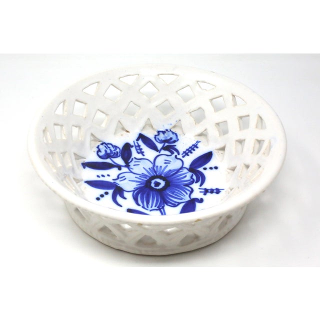 A vintage, handmade ceramic bowl, with a cutout/basket weave design and hand-painted blue flower and foliage.