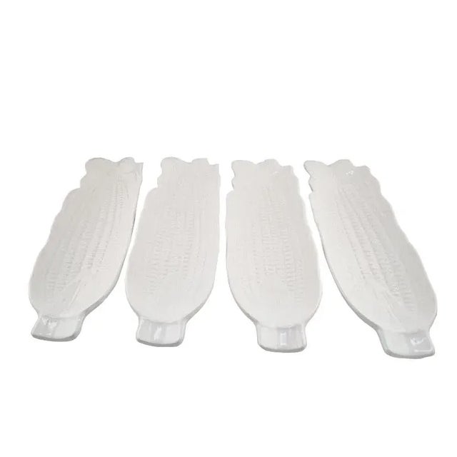 A charming set of four vintage white ceramic corn-on-the-cob holders, each shaped like an ear of corn with finely molded...