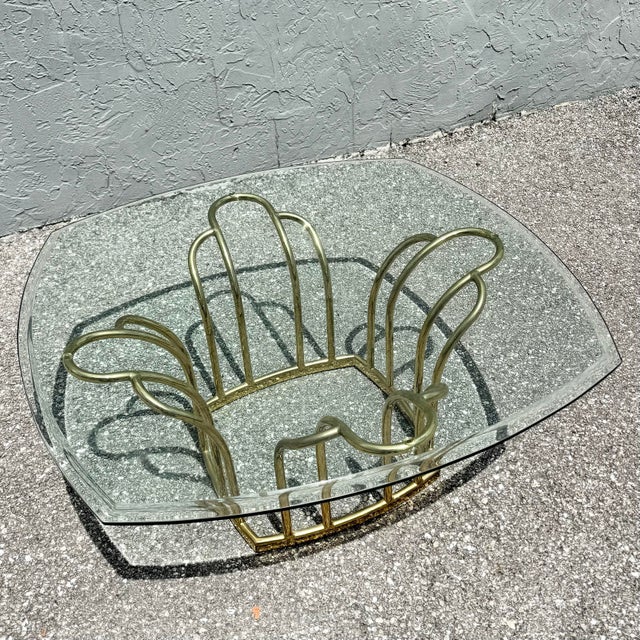 Distinctive Art Deco style coffee table featuring a sculptural brass-tone metal base paired with a beveled glass top. The...