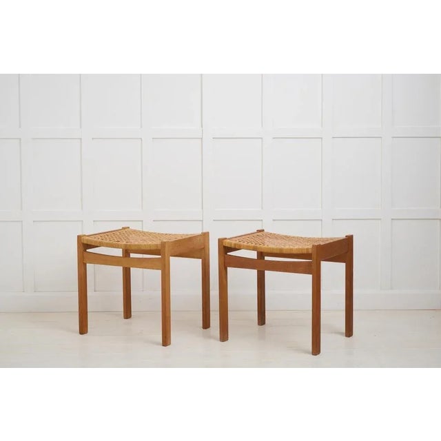 A pair of Danish design footstools, with a frame in solid oak and a seat in rattan. One stool has a sticker from Illums...