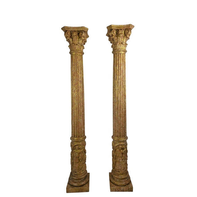 A pair of tall carved and gilded wooden columns, circa 1920. Each column rises from a square plinth to a fluted shaft and...