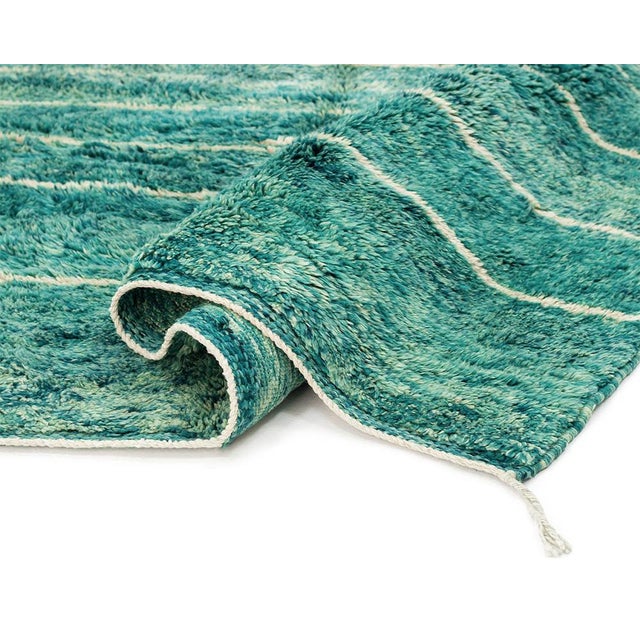 A rug that moves like water — horizontal bands of emerald and blue melt into one another, threaded through with fine cream...