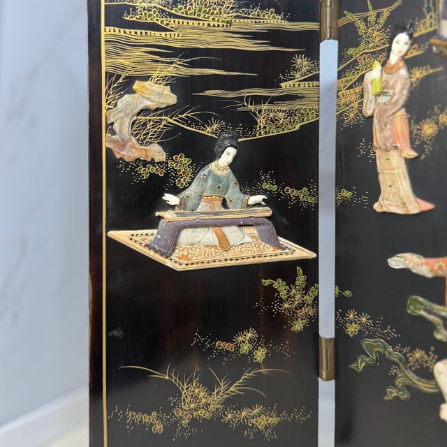 A mid‑20th‑century Japanese tabletop byōbu screen with four lacquered wood panels joined by brass hinges. One side shows...