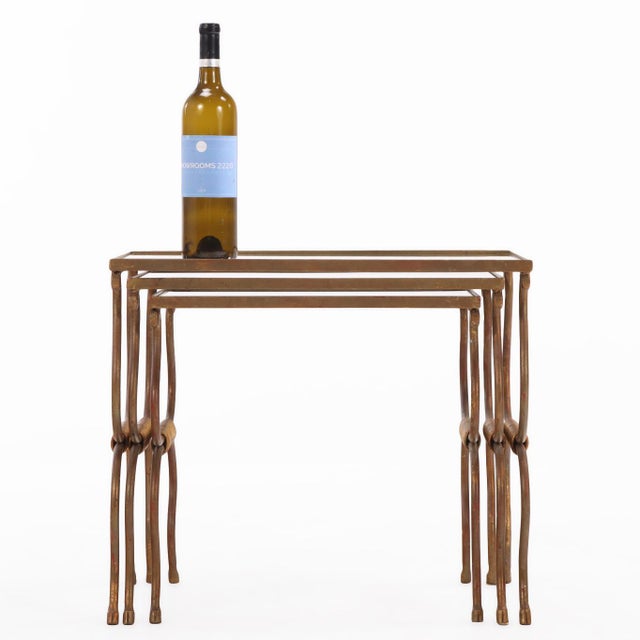A set of French gilt iron nesting tables, circa 1950, featuring slender metal frames with a gilt finish and inset glass...