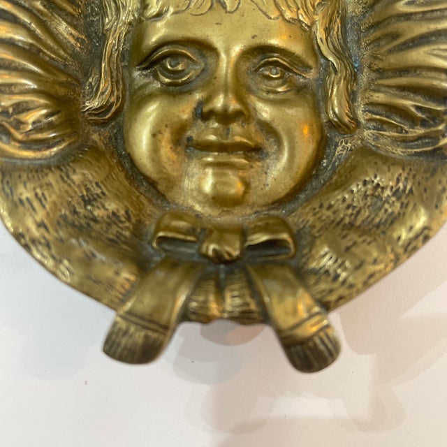 This vintage solid brass decorative dish features a detailed relief portrait of a young girl wearing a bonnet tied with a...