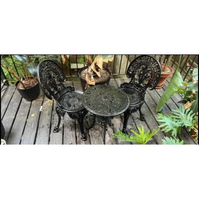 An exceptionally charming and substantial cast iron bistro set featuring an intricately detailed round table and two...