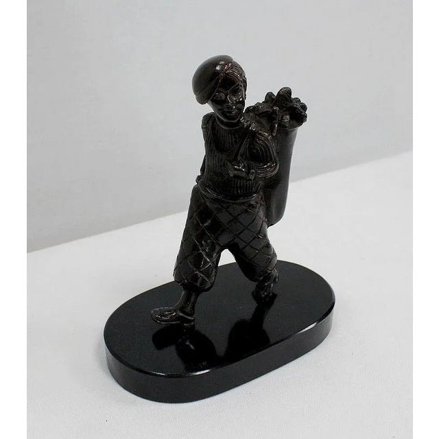 Bronze with brown patina on a black marble base representing a young caddy carrying a golf player's bag. Smiling, this...