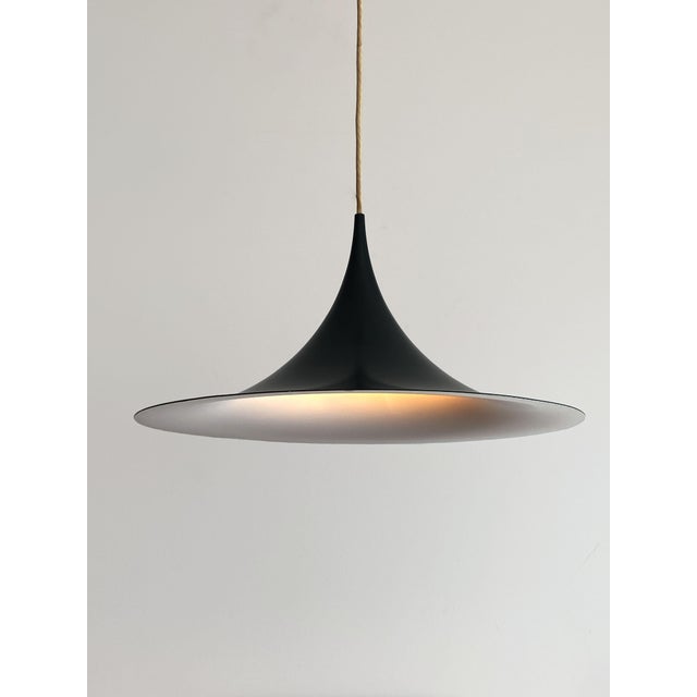When lit, the white interior reflects a soft, even glow down onto the table below, while the dark petrol-grey outside...