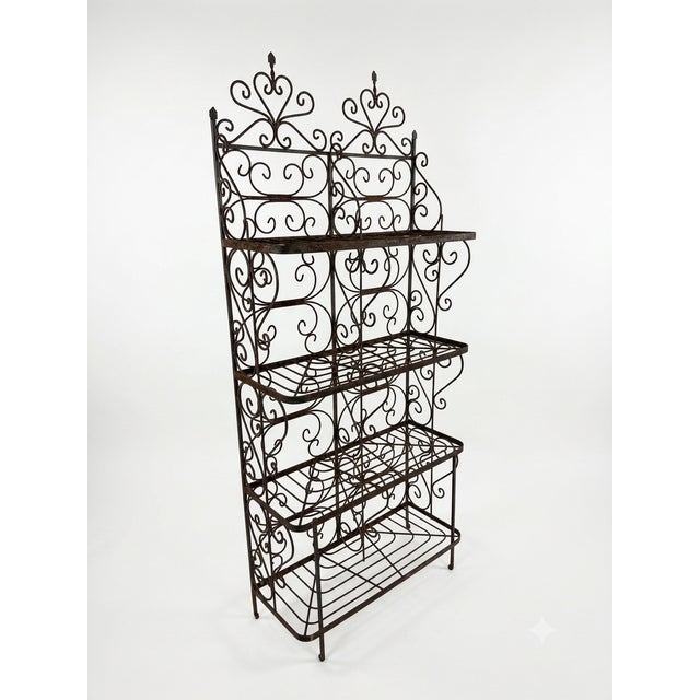 Elegant vintage wrought iron étagère featuring ornate scrollwork, fleur-de-lis finials, and a rich aged patina. This four-...