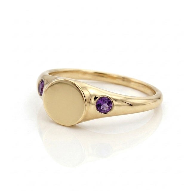 A timeless classic with a touch of royal charm. This signet ring showcases an unadorned, flat oval plate flanked by two...