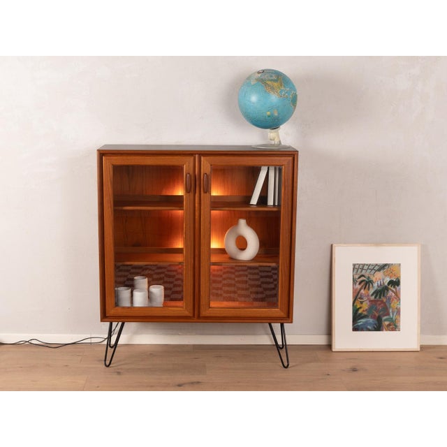 Classic showcase from the 1960s. Corpus in teak veneer with two glass doors, two shelves and new hairpin legs in black....